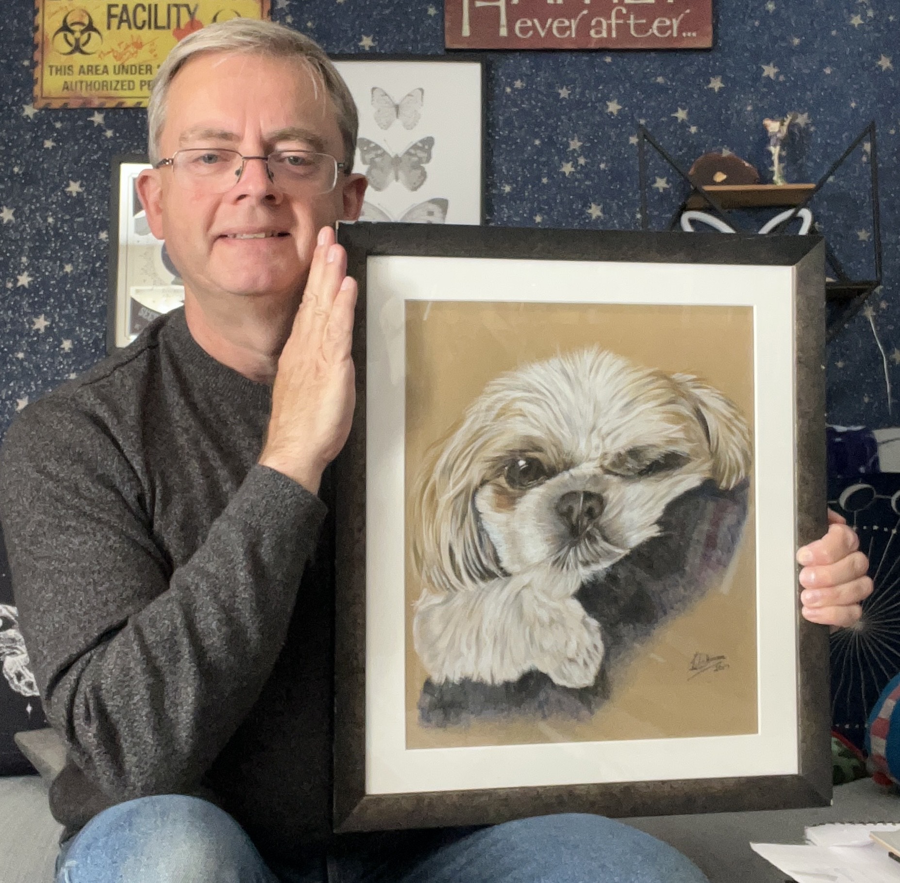Lee a white man is sitting holding up a pencil drawing he did of our dog Gizmo a white and tan shih tzu
